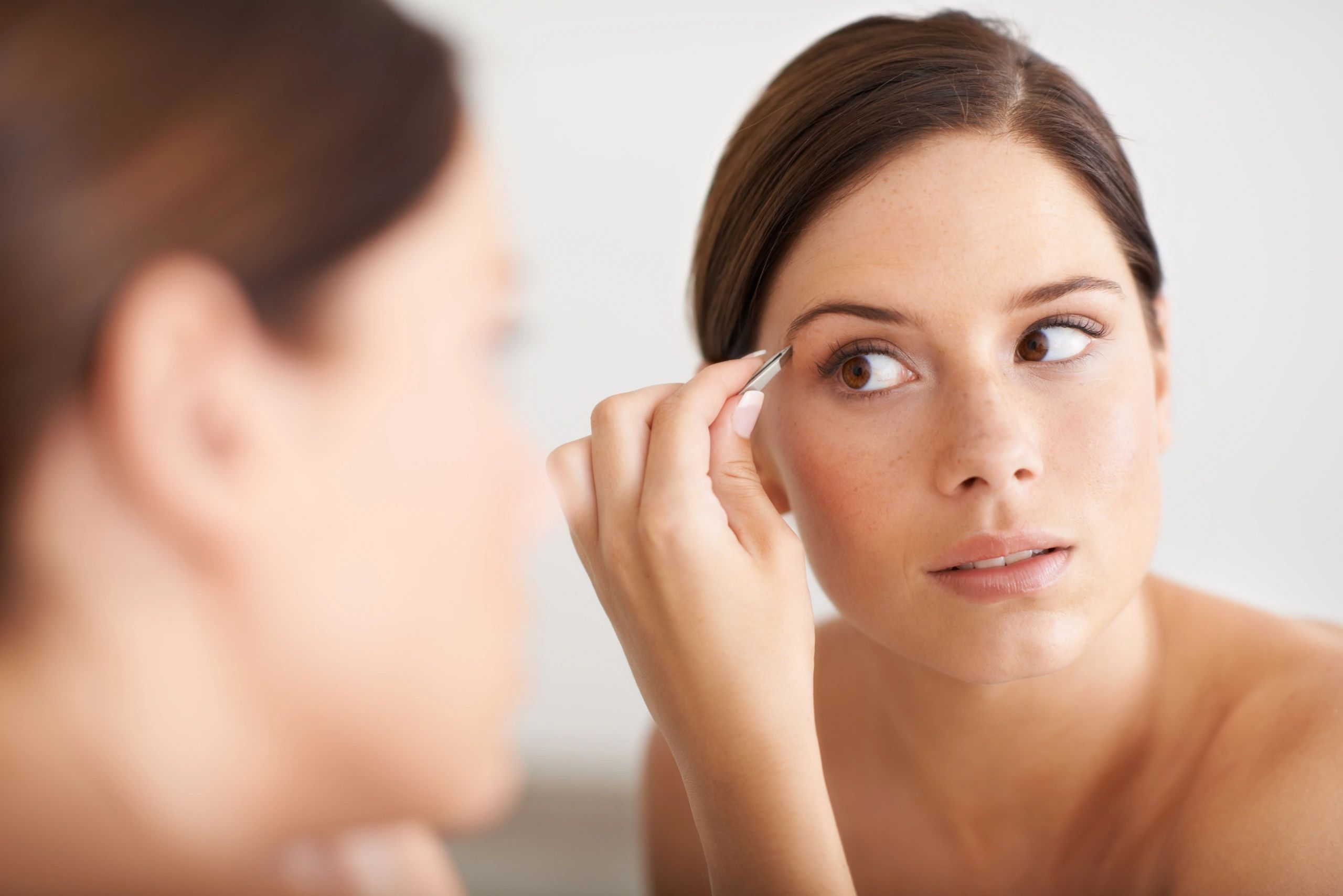 Client grooming brows in mirror